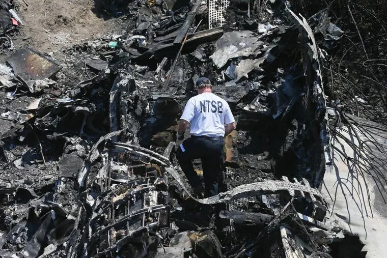 A National Transportation Safety Board official looks through the wreckage at the scene Monday, June 2, 2014, in Bedford, Mass., where a plane plunged down an embankment and erupted in flames during a takeoff attempt at Hanscom Field on Saturday night. Lewis Katz, co-owner of The Philadelphia Inquirer, and six other people died in the crash. (AP Photo/Boston Herald, Mark Garfinkel, Pool)