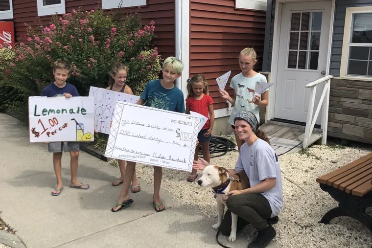 "Kitty Lovers" club members (from left to right) Keegan Fields, Mairin Fields, Miles Newdeck (holding the check), Margot Fields, Sophie Newdeck, and Katie Bailey, employee of Humane Society of Ocean City, posing with Levi the dog. The members of the club presented Bailey with the handmade check for $150 outside the Humane Society of Ocean City on Aug. 17.