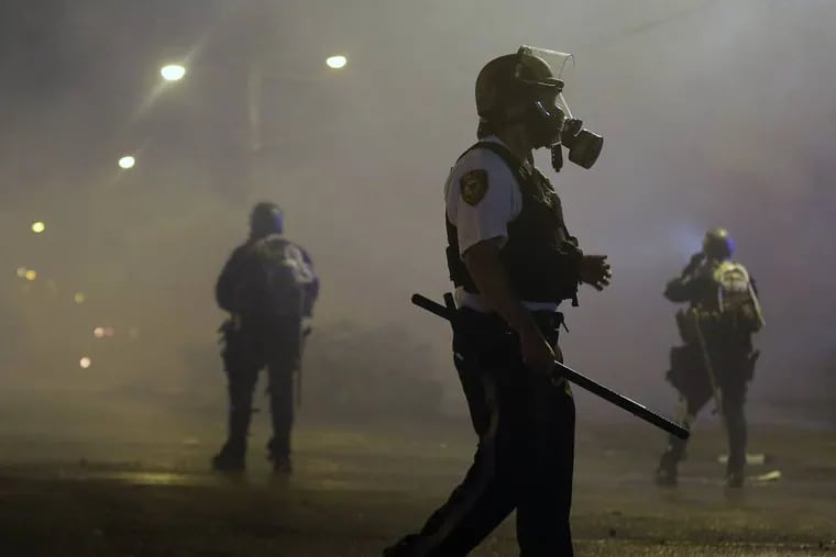 Law enforcement officers wait to advance Sunday, Aug. 17, 2014, after firing tear gas to disperse a crowd protesting the shooting of teenager Michael Brown last Saturday in Ferguson, Mo. Brown's shooting in the middle of a street following a suspected robbery of a box of cigars from a nearby market has sparked a week of protests, riots and looting in the St. Louis suburb. (AP Photo/Charlie Riedel)