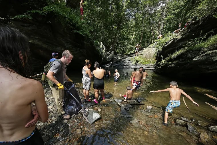Shawn Green, a volunteer with Friends of the Wissahickon, picks up litter as visitors cool off at Devil’s Pool in Wissahickon Valley Park. People are warned not to swim in the water, but it’s a losing battle.