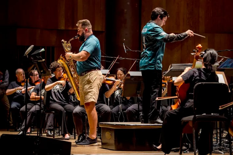 Philadelphia Eagles center Jason Kelce (left) plays his baritone saxophone with the Philadelphia Orchestra performing the Eagles Fight Song onstage at the Mann Center July 24, 2018. The orchestra, NFL Films, and the Philadelphia Eagles celebrated the Super Bowl Season with the world premiere of a "Philly Special" concert and video event. At right is conductor Aram Demirjian.
