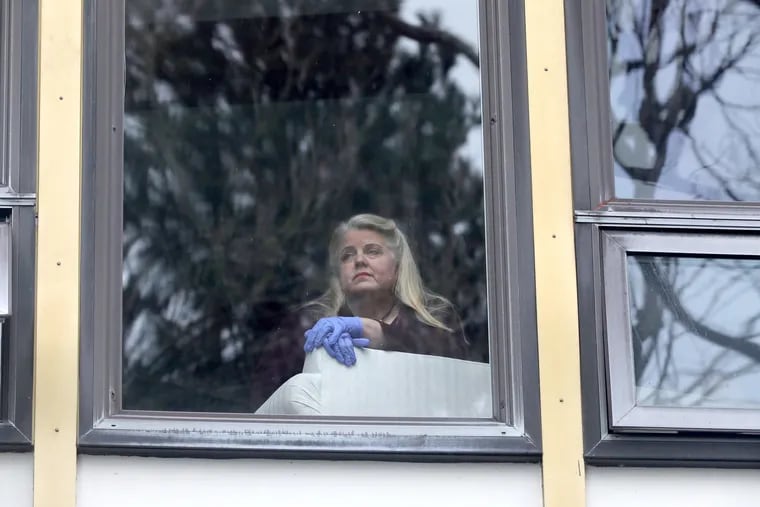 Wearing rubber gloves, retired choir director Carleigh Bedell is self-isolating due to concerns about COVID-19 and because she is at higher risk due to underlying health conditions. She peers out her second floor apartment window.