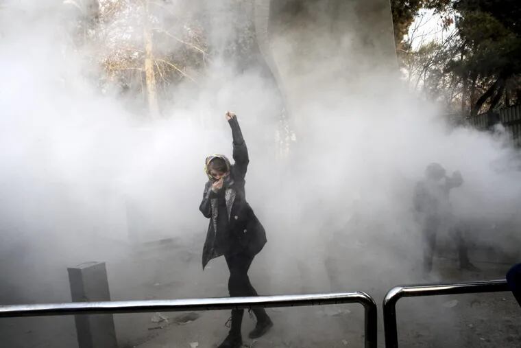 In this Saturday, Dec. 30, 2017 file photo taken by an individual not employed by the Associated Press and obtained by the AP outside Iran, a university student attends a protest inside Tehran University while a smoke grenade is thrown by anti-riot Iranian police, in Tehran, Iran. Iran has seen its largest anti-government protests since the disputed presidential election in 2009, with thousands taking to the streets in several cities in recent days.