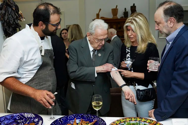 Holocaust survivor Steven Fenves, with chef Alon Shaya (left), shows a prisoner number tattooed on his arm at Auschwitz to guests at a June 2022 fundraising dinner for the United States Holocaust Memorial Museum in Washington, D.C.