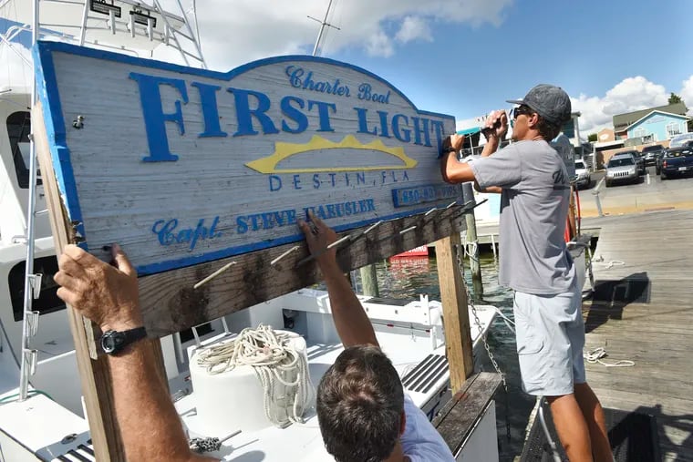 Capt. Steve Haeusler, left, and Wyatt Ferreira take down the sign for Haeusler's charter fishing boat "First Light" on Monday, Oct. 8, 2018. Boat captains in this fishing community were relocating their vessels to safer locations in advance of Hurricane Michael.