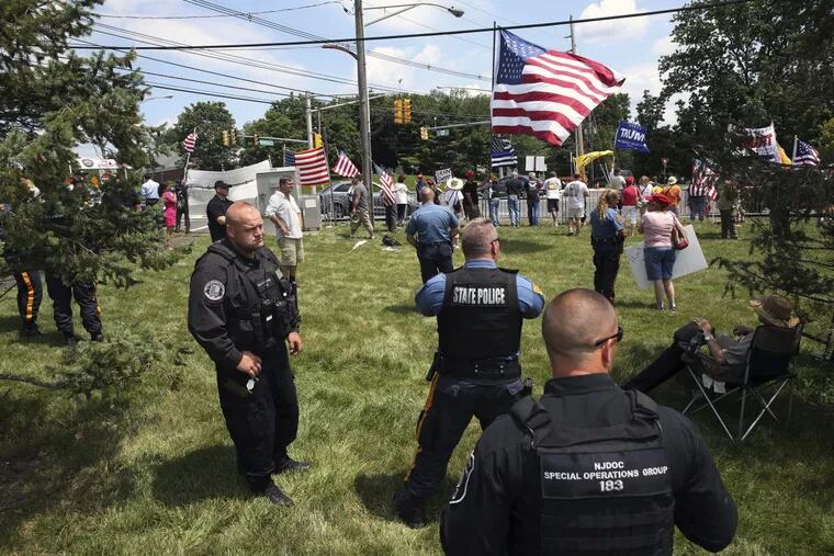 Police officers stand near as groups of President Donald Trump supporters and protesters wave flags and signs at passing motorists during gatherings not far from Trump National golf course, where Trump was attending the Women’s US Open tournament, Saturday.