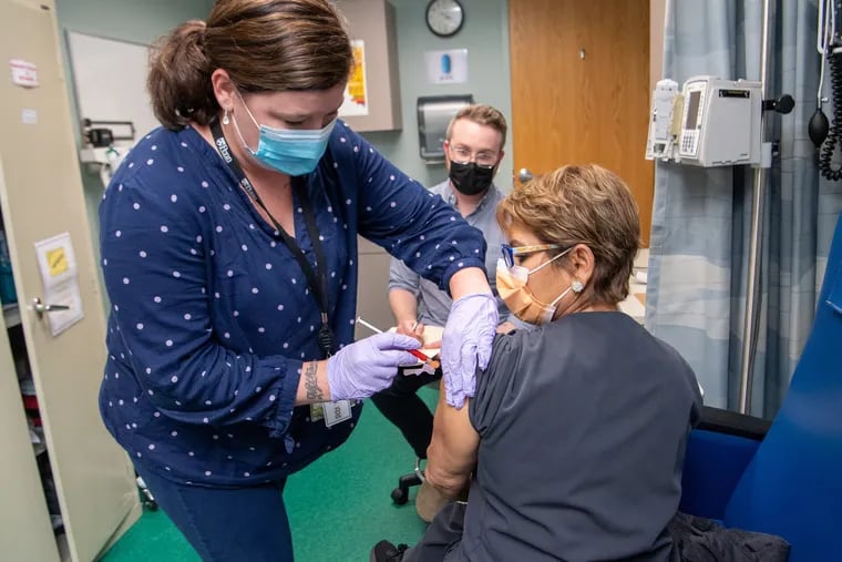 Nicole Kordziel gives Enelida Gomez, a nurse in Philadelphia, an investigational COVID-19 vaccine as part of the clinical trial for Moderna’s mRNA vaccine at Penn Medicine in October. Seated in back is William Vickroy, a research nurse at Penn.