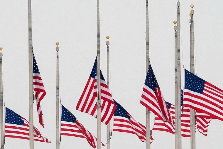 Visitors walk past flags at half-staff near the Washington Monument in Washington. Associated Press