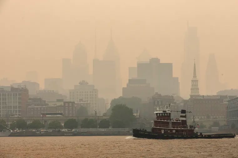 A tugboat goes down the Delaware River as smoke from Canadian wildfires casts a haze against the Philadelphia skyline. 