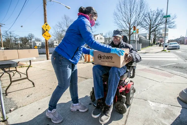 Pennsylvania State Representative Donna Bullock, left, places a box of canned goods into the lap of Marvin Smith, right, who came to collect his case of food, in his motorized wheel chair, on Thursday morning, April 2, 2020.  Because of the spread of the coronavirus, 400 hundred cases of food were distributed to area residents at the at the Hank Gathers Memorial Recreation Center at 2501 Diamond Street for April 2, 2020. 100 cases of fresh produce and 300 cases of canned goods. Only one case per family. The cases were gone in 30 minutes.