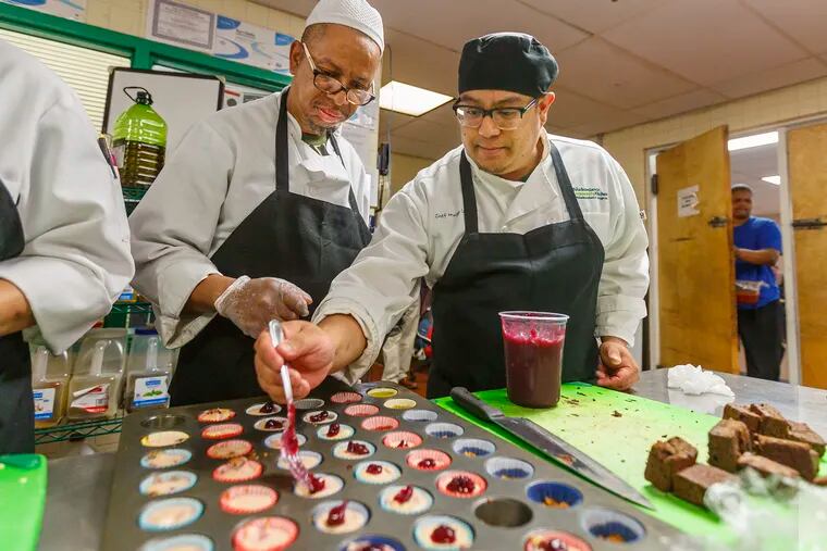 At Philabundance Community Kitchen, chef Hugo Campos, right, shows culinary student Charles Jones  the correct procedure for placing cranberries on small cheesecake cupcakes on May 1.