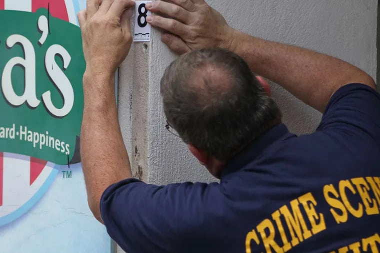 Police Sgt. Steve Crosby numbers one of the 10 holes in the facade of the building that houses the Rita's Water Ice on Girard Avenue where a security gate crushed and killed Wynter Larkin during a fund-raising event Saturday.