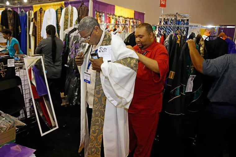 The Rev. John L. Dees Jr. from Mobile, Ala., tries on a preacher's robe with the help of the Rev. Willis Camp III at the Robes of Faith booth in the expo hall of the Pennsylvania Convention Center.