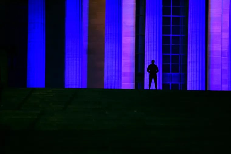 April 13, 2020: A lone figure pauses at the top of the "Rocky Steps" at the Philadelphia Museums of Art as the city lights the night blue to honor health-care workers fighting on the front lines of the coronavirus pandemic