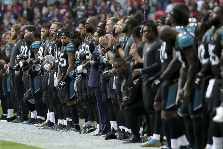 Jacksonville Jaguars owner Shahid Khan (center) joins arms with players as some kneel during the playing of the U.S. national anthem before an NFL game against the Baltimore Ravens at Wembley Stadium in London.