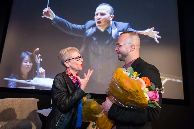 Terry Gross, left, and Yannick Nezet-Seguin talk after taping an interview for a Fresh Air segment in front of a live audience at WHYY on April 2, 2019. A video of Yannick conducting is projected in the background.