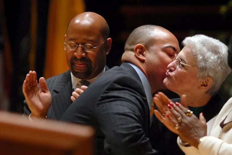 As former Mayor Michael Nutter (left) applauds, Seth Williams kisses outgoing DA Lynne M. Abraham (right) immediately after he is sworn in as district attorney at a ceremony at the Kimmel Center Jan. 4, 2010. Abraham filed a joint lawsuit Monday to have Williams removed from office.