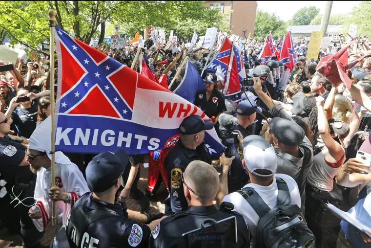 Members of the Ku Klux Klan are escorted by police past a large group of protesters during a rally in Charlottesville, Va.