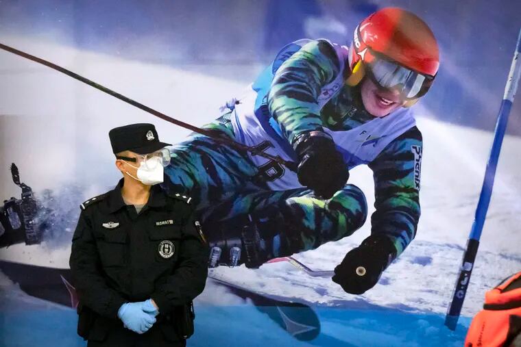 A police officer wearing a face mask and goggles to protect against COVID-19 stands near a poster of a skier on the wall at a train station in Zhangjiakou in northern China's Hebei Province.