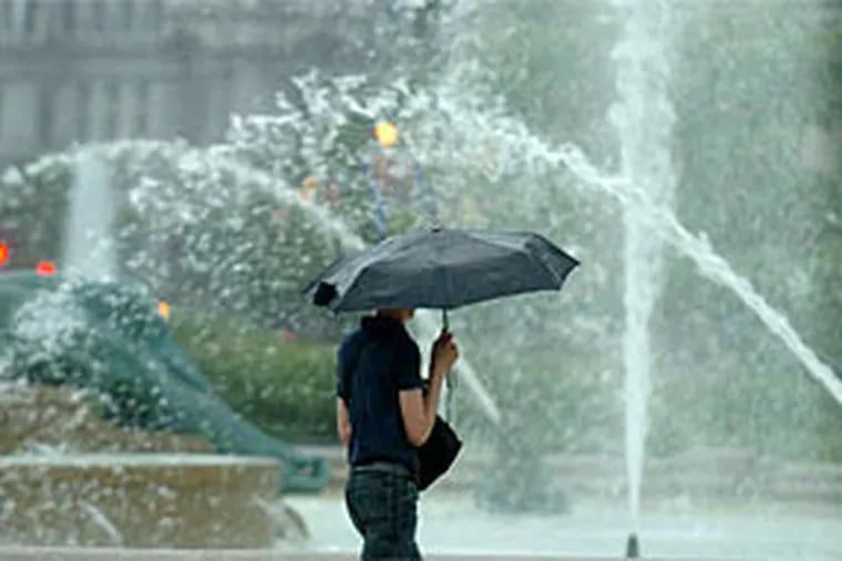 In an appearance that's only slightly deceiving, a woman seems to walk through Swann Fountain on Logan Circle. She was not in the fountain, of course. But it no doubt felt that way during yesterday's showers. (Clem Murray / Staff Photographer)