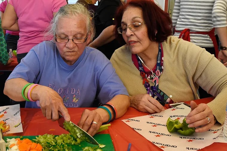 Carmen Figueroa practices her slicing skills after the chefs’ demonstration, as her friend Carmen Laureano watches. One participant says the classes have made her more aware of what she buys at the grocery, including, for the first time, kale.