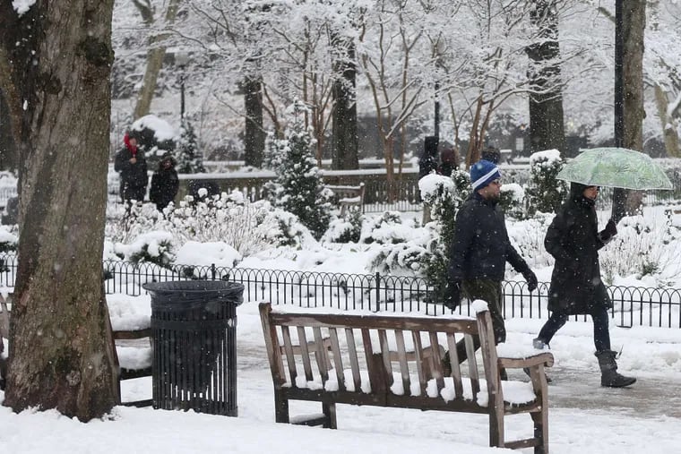 People walk through Rittenhouse Square as snow falls on Wednesday.
