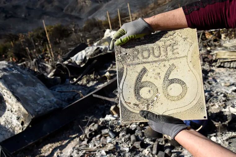 Donna Phillips shows a charred Route 66 sign she found among the possessions of her friend Marsha Maus on Sunday after wildfires tore through the Seminole Springs Mobile Home Park in Agoura Hills, Calif.