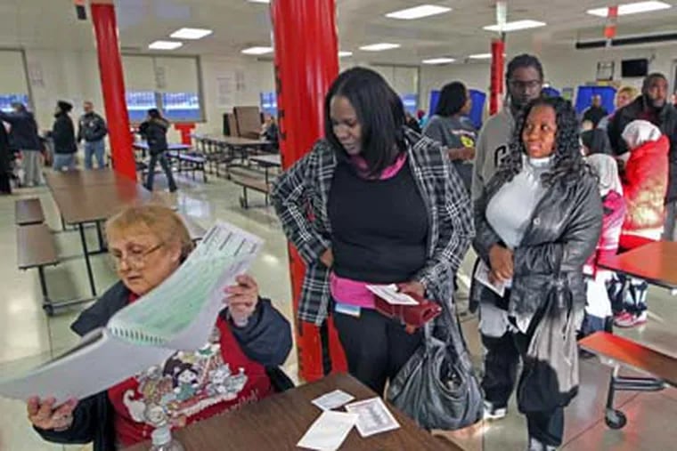 As the lines start to get longer in the afternoon, poll worker Kathy Barfield, left, looks to find the name of Kimberly Knight, center, so she can vote at Benjamin Franklin Elementary School  A mural of President Barak Obama had to be covered in the school cafeteria of Benjamin Franklin Elementary School,  after Republicans got a judge to issue an order that it must be covered so those people voting could not see the President's image as they waited to vote.  (Michael Bryant / Staff Photographer)