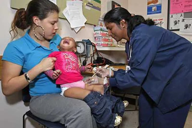 Hazelline Torres (left) holds her daughter Emery Torres as RN Saji Philip administers a shot at the city's District Health Center. ( Michael S. Wirtz / Staff Photographer )
