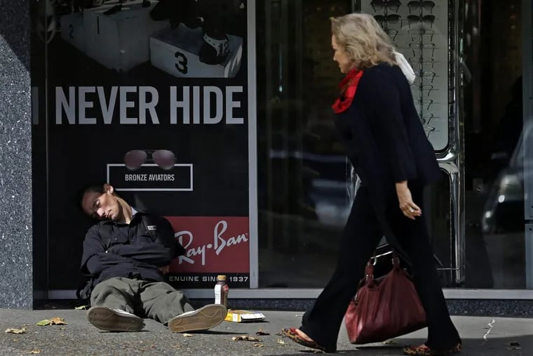 A pedestrian walks past a man sleeping on a public sidewalk in downtown Portland, Ore., where the number of homeless have been rising.