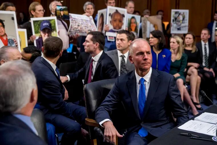 In this Oct. 29, 2019, file photo Boeing Company President and Chief Executive Officer Dennis Muilenburg, right foreground, watches as family members hold up photographs of those killed in the Ethiopian Airlines Flight 302 and Lion Air Flight 610 crashes during a Senate Committee on Commerce, Science, and Transportation hearing on Capitol Hill.