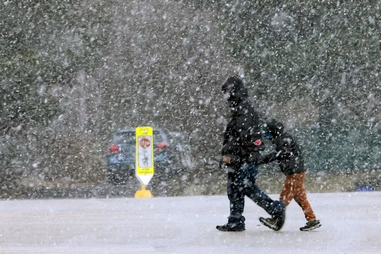 Pedestrians walk through the snow on Monday evening. While many suburban districts delayed opening schools or closed altogether, and the Archdiocese of Philadelphia ordered its schools to pivot to a remote learning day, the Philadelphia School District opened on a normal schedule, frustrating many.