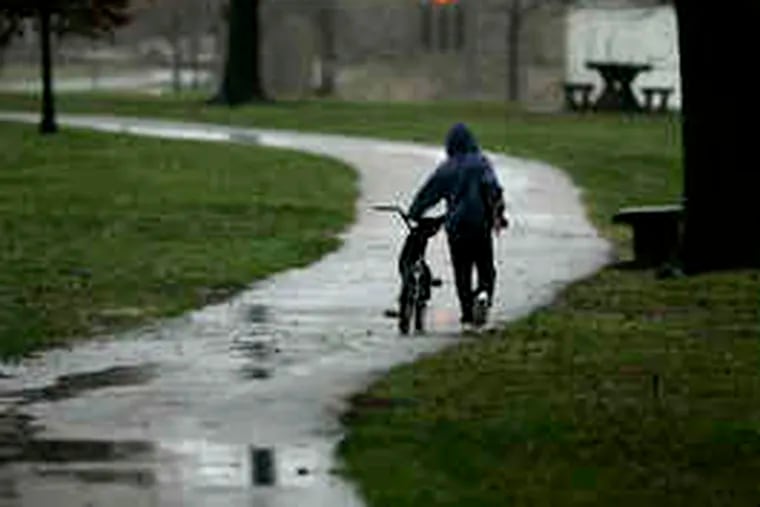 A cyclist walks his bike through FDR Park. The region was left sopping wetby the combination of melting snow and persistent rain. The National Weather Service expected the rain to end this morning.