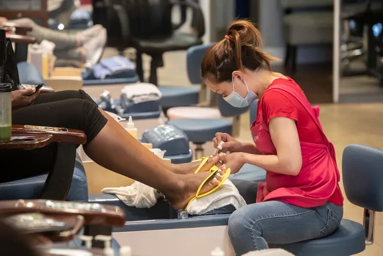 One of the employees at Tran Nail Salon, in the Bala Cynwyd Shopping Center on City Line Avenue in Montgomery County, who is wearing a mask, works on a customer's pedicure on Sunday, March 15, 2020.