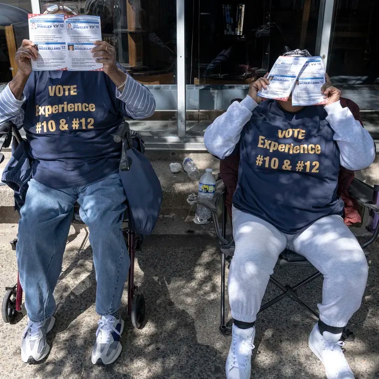 Two unidentified volunteers cover their faces with pamphlets as they hand them out to voters outside the Fleisher Art Memorial election polling place, in South Philadelphia.