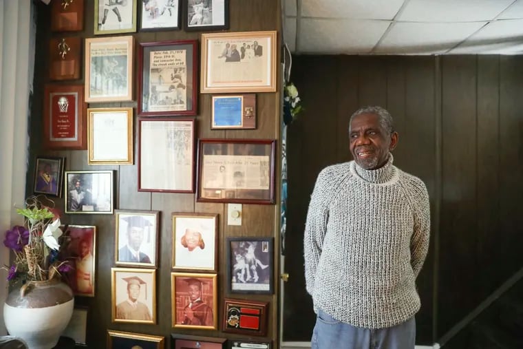 Carl Lacy poses next to a wall of old basketball clippings featuring him and his family at his home in West Philadelphia.