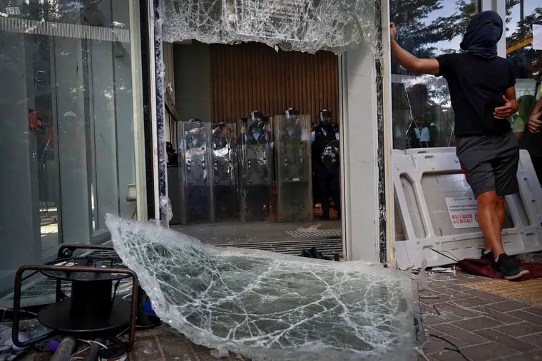 Police officers with shields stand guard behind the damaged glass of the Legislative Council in Hong Kong after protesters tried to break in.