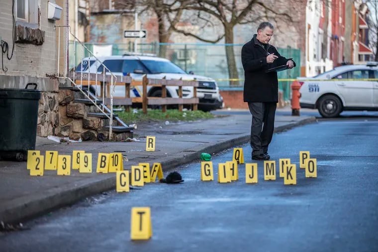 A Philadelphia Police investigator stands on the 2400 block of North Patton Street in the Strawberrry Mansion section of Philadelphia surrounded by multiple shell casings where two men were shot early Sunday morning. Police said they have two men in custody.