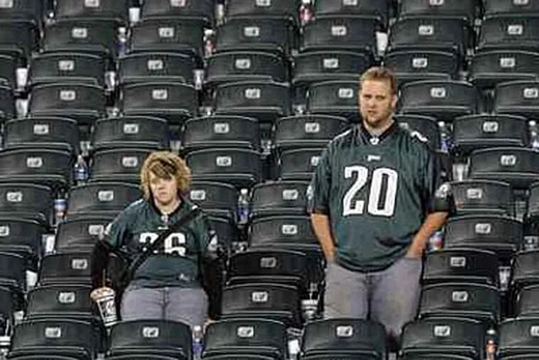 The seats everybody wants, except after an Eagles loss. Two dejected fans stand amid rows of empty seats after the team's last-minute loss to Chicago in October. (Jerry Lodriguss/Inquirer)