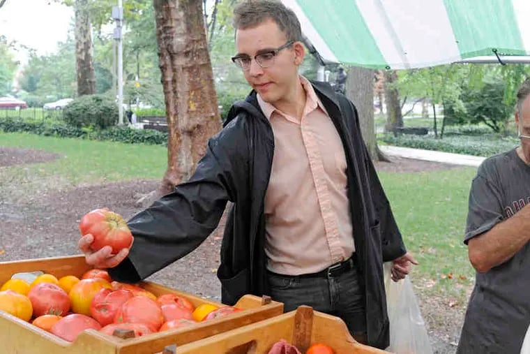 Bench Ansfield, a Philly Food Bucks user, picks up a tomato at Clark Park in West Philadelphia. The pilot effort provides $2 in vouchers for every $5 spent on produce at Food Trust markets.