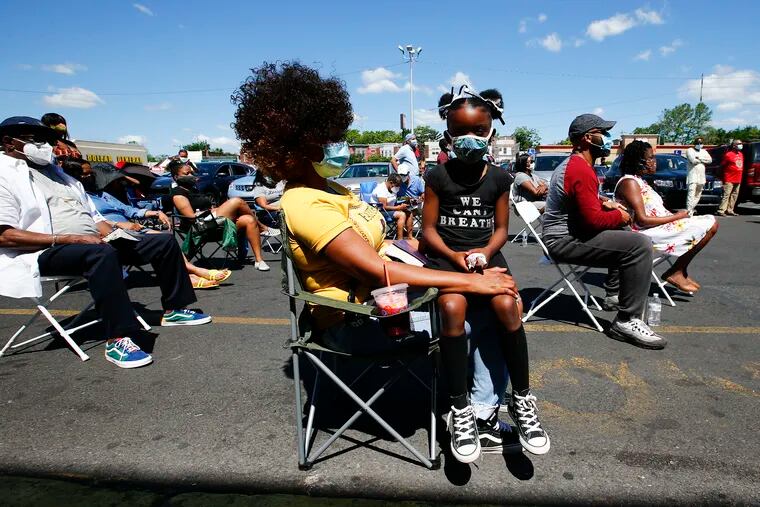 Lyric Williams, 7, sits on the lap of her mother Latasha Williams during an outside sermon conducted by the Salt and Light Church at the Woodland Village Plaza.