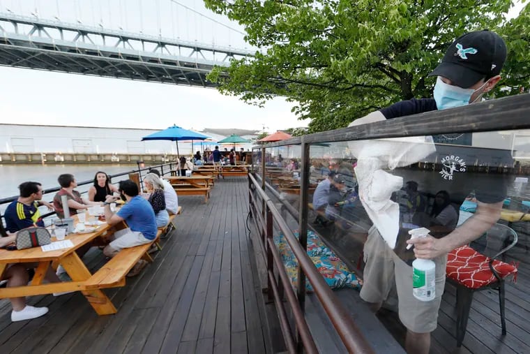At Morgan’s Pier on the Delaware River, runner Gabriel Ritter (right) cleans a plexiglass partition that was installed prior to their re-opening on June 12, 2020. Outdoor dining is now allowed as Philadelphia moves into the yellow phase of the re-opening due to the coronavirus (COVID-19) pandemic.