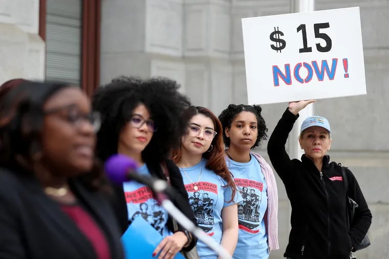 Myriam Ramirez (right) holds up a sign during a rally to raise the state and local minimum wage in Philadelphia, Pa., on Tuesday, May 9, 2023. Philadelphia Councilmember Kendra Brooks (left) addresses the group.