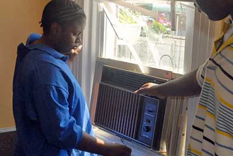 Shamika and Dan King install a donated air conditioner in a living-room window. (Ron Tarver/Inquirer)