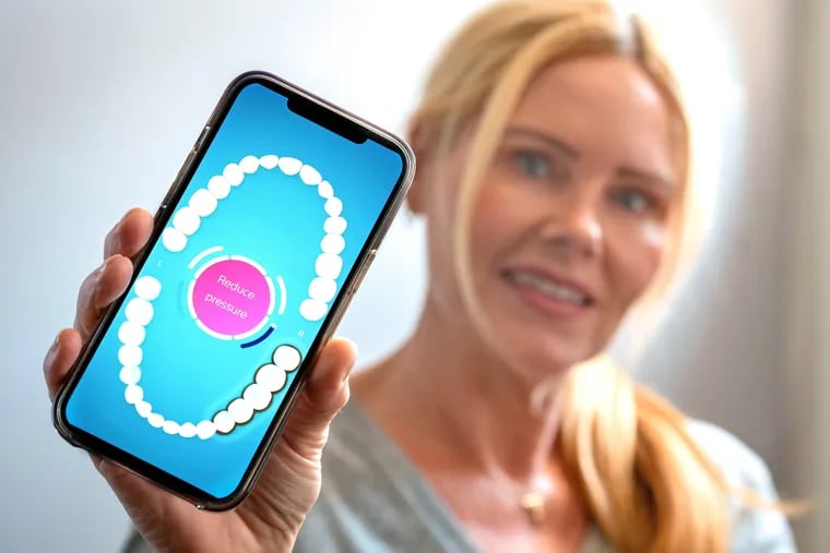 Colleen Rex poses June 30, 2022 with a phone app which connects to her artificial intelligence-enabled electric toothbrush, to tell her when she missed a spot or is brushing too hard against her gums.