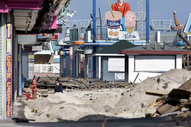 FILE - In this Nov. 22, 2012 file photo, a woman walks past debris from the damaged boardwalk in Seaside Heights, N.J.  Heavy equipment including a gigantic drill and a pile-driving machine were brought onto the sand in the south end of town Friday, Feb. 15, 2013, as workers began drilling holes in the sand and pounding wooden pilings into them, shaking the ground for blocks around. It marked the beginning of a $3.6 million contract the borough awarded to rebuild the boardwalk. Mayor William Akers said the initial work, restoring the boardwalk so that it can be walked on safely, should be done by May 10. Railings, lighting and ramps will be part of a second contract that has yet to be awarded. The project is also likely to include a protective seawall, and cost between $6 million and $7 million, the mayor said. (AP Photo/Mel Evans, File)