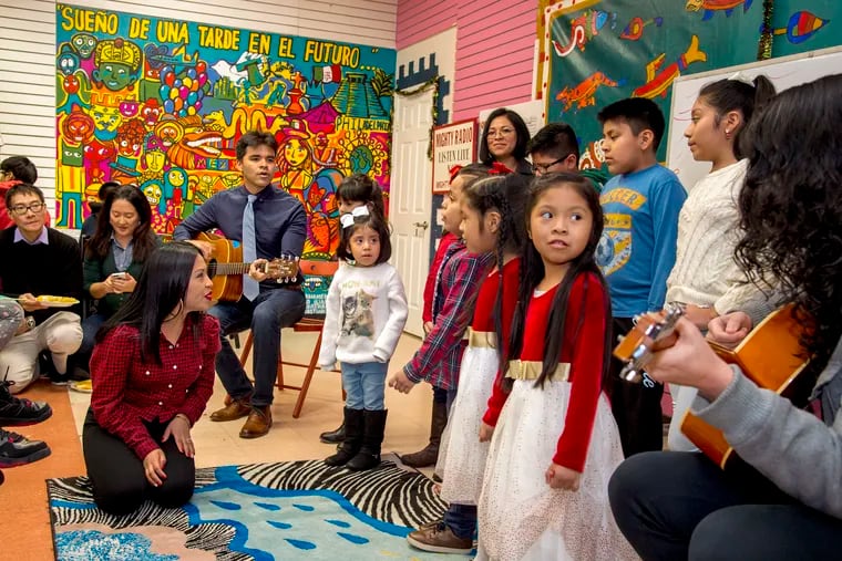 Program manager Mario Meza (rear) plays guitar and Reyna Hernandez (kneeling) help the children sing for family and friends at the Christmas Party of the Mighty Writers El Futuro Branch on South Ninth Street.