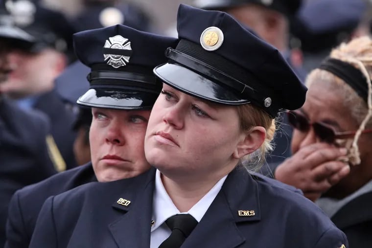 Philadelphia firefighter Jacquie Packard, left, rests her head on fellow firefighter Brittney Kern-Hughes' shoulder as they both watch the funeral services. ( Michael Bryant / Staff Photographer )
