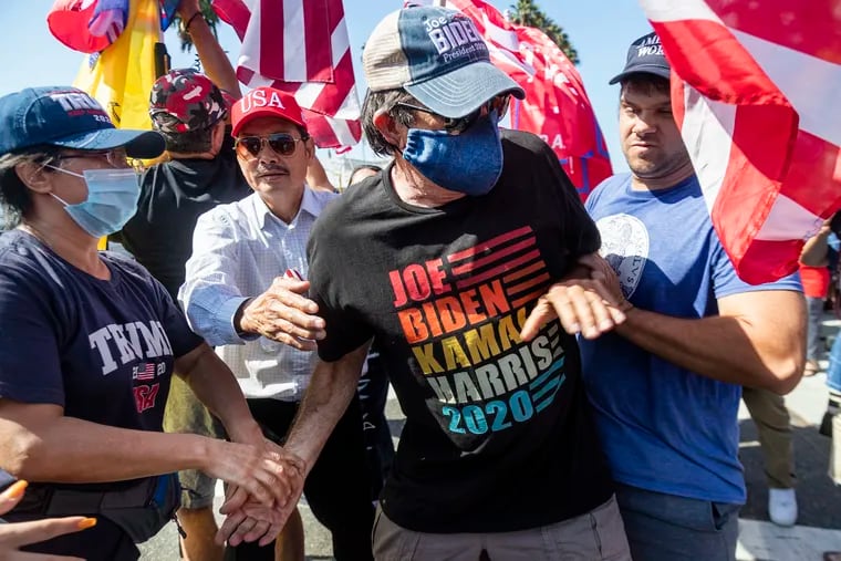Joe Biden supporter Richard Williams, 70, of Irvine is grabbed and shoved by Trump supporters as tried to hold his Biden-Harris sign amid a sea of Trump supporters who gathered on Via Lido to get a glimpse of the president's motorcade while going to and from a Newport Beach fundraiser. (Gina Ferazzi/Los Angeles Times/TNS)