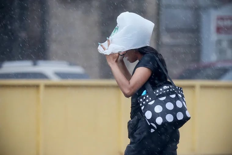 A woman covers her head with a plastic bag during a downpour as she crosses Erie Avenue at Germantown Avenue in North Philadelphia on Wednesday, Aug. 7, 2019.